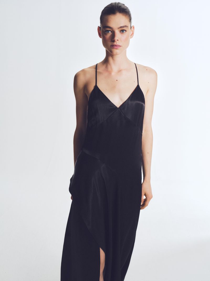 Model wearing a black slip dress against a plain white studio background