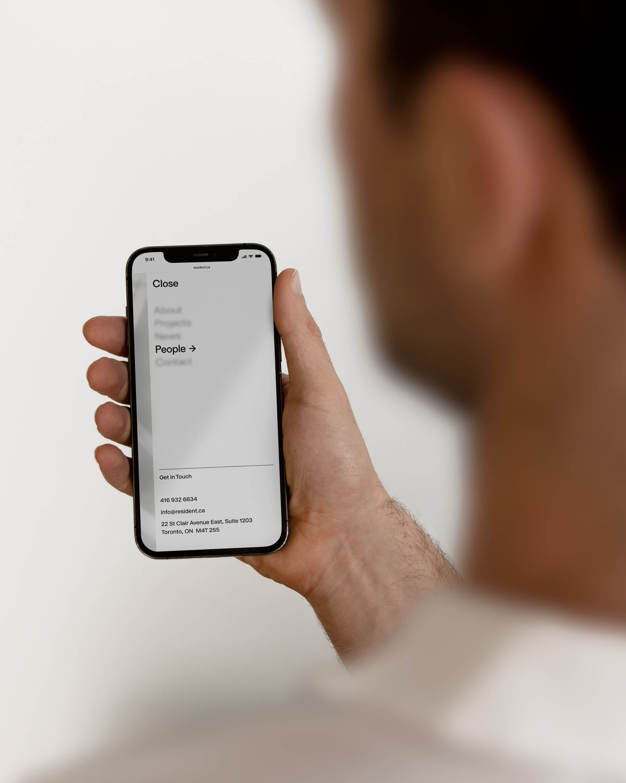 Close-up of a person holding a smartphone, displaying a menu with options like 'About', 'Projects', and 'People'.