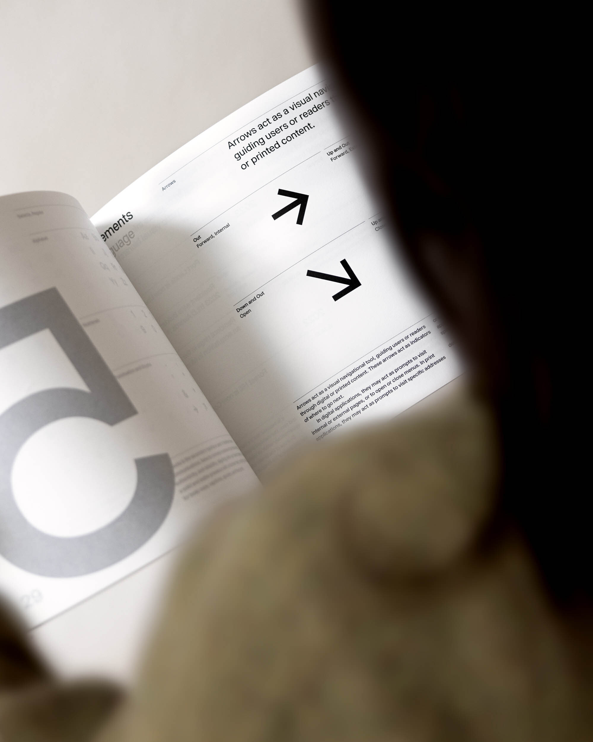 Open book with arrows pointing to written text; a person looks on. Book provides visual navigation for guiding users or readers.