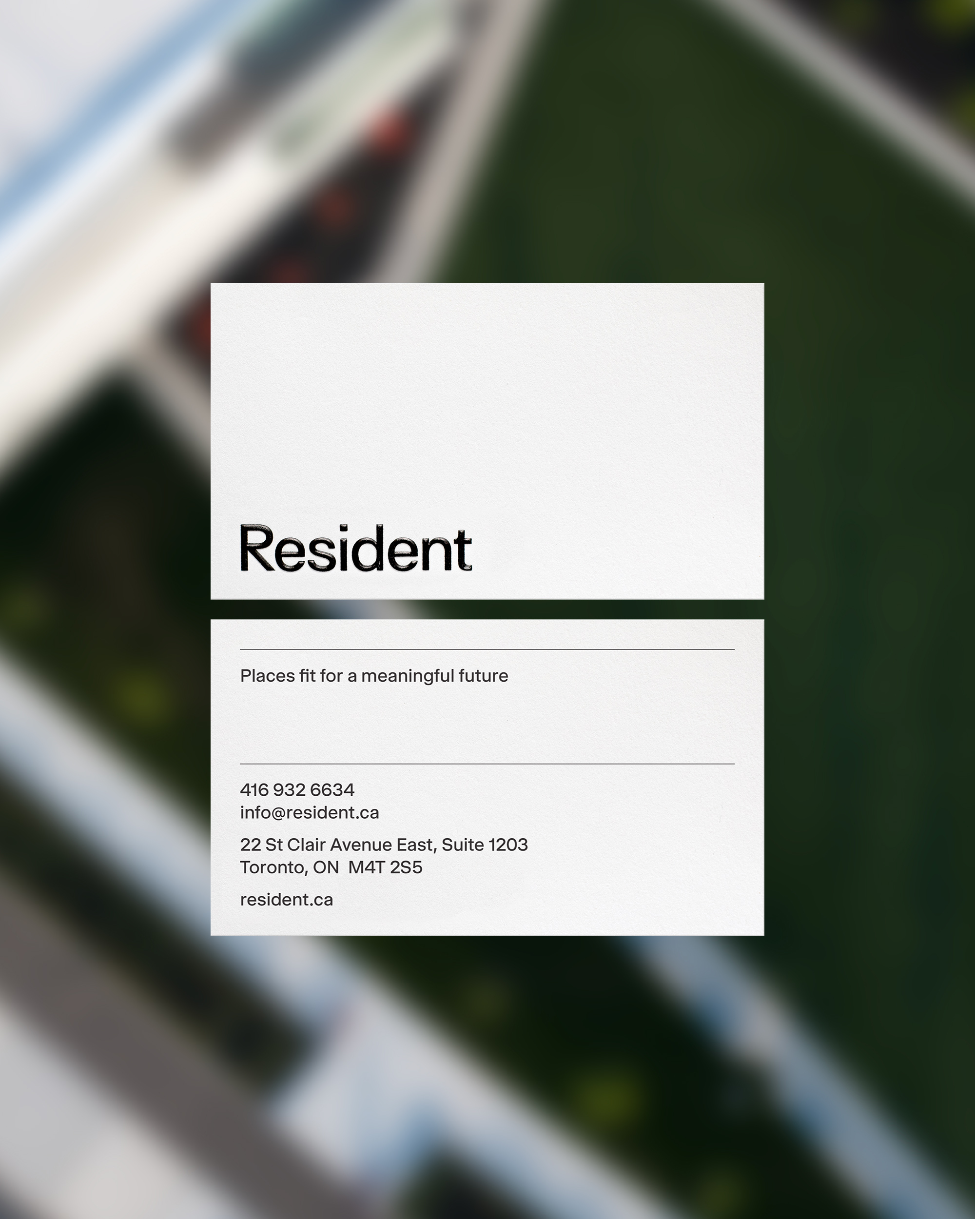 Close-up of a white business card featuring the name 'Resident,' company contact information, and a blurred background with greenery.