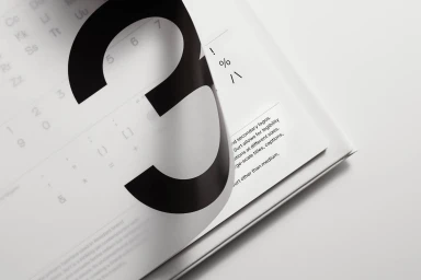 Curling corner of a printed white page revealing a large black number three and typographical guidelines.