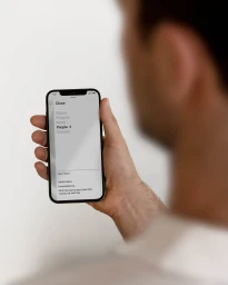 Man holding a black smartphone showing website navigation against a plain white background for Resident brand identity