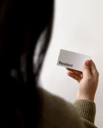 Close-up of a person holding a white business card featuring the Resident logo against a plain wall.