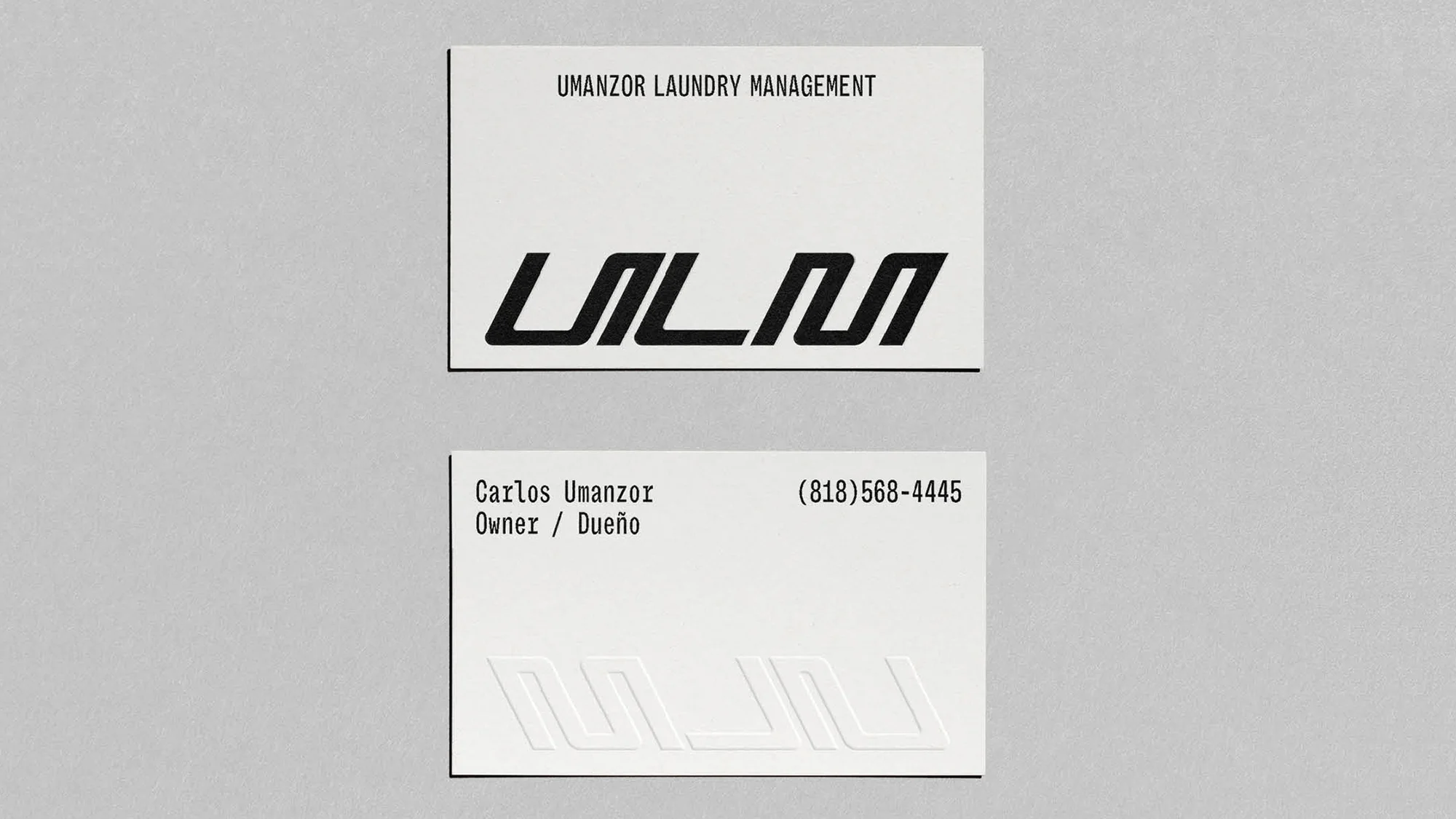 Two business cards on a gray surface. The cards feature a modern, stylized logo and contact information for Umanzor Laundry Management.