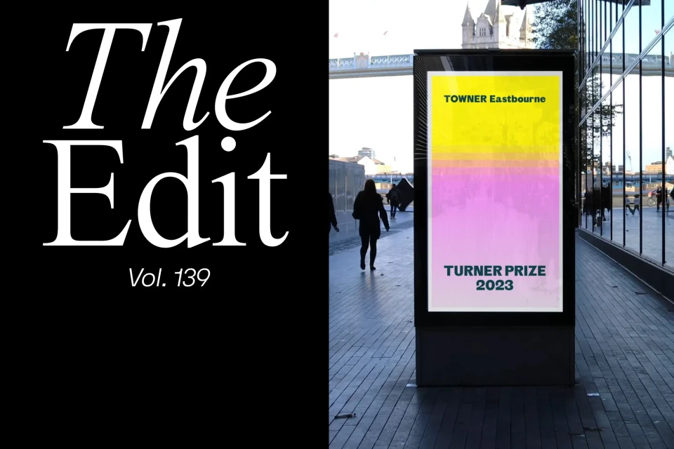 Outdoor billboard in London promotes the Turner Prize 2023, featuring yellow and pink graphic art and pedestrians in the background.