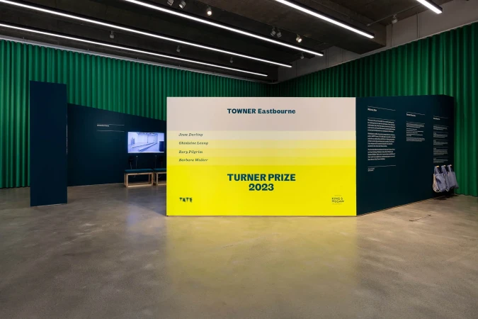 Interior view of the Turner Prize 2023 exhibition at Towner Eastbourne, featuring text panels and a monitor displaying artwork.