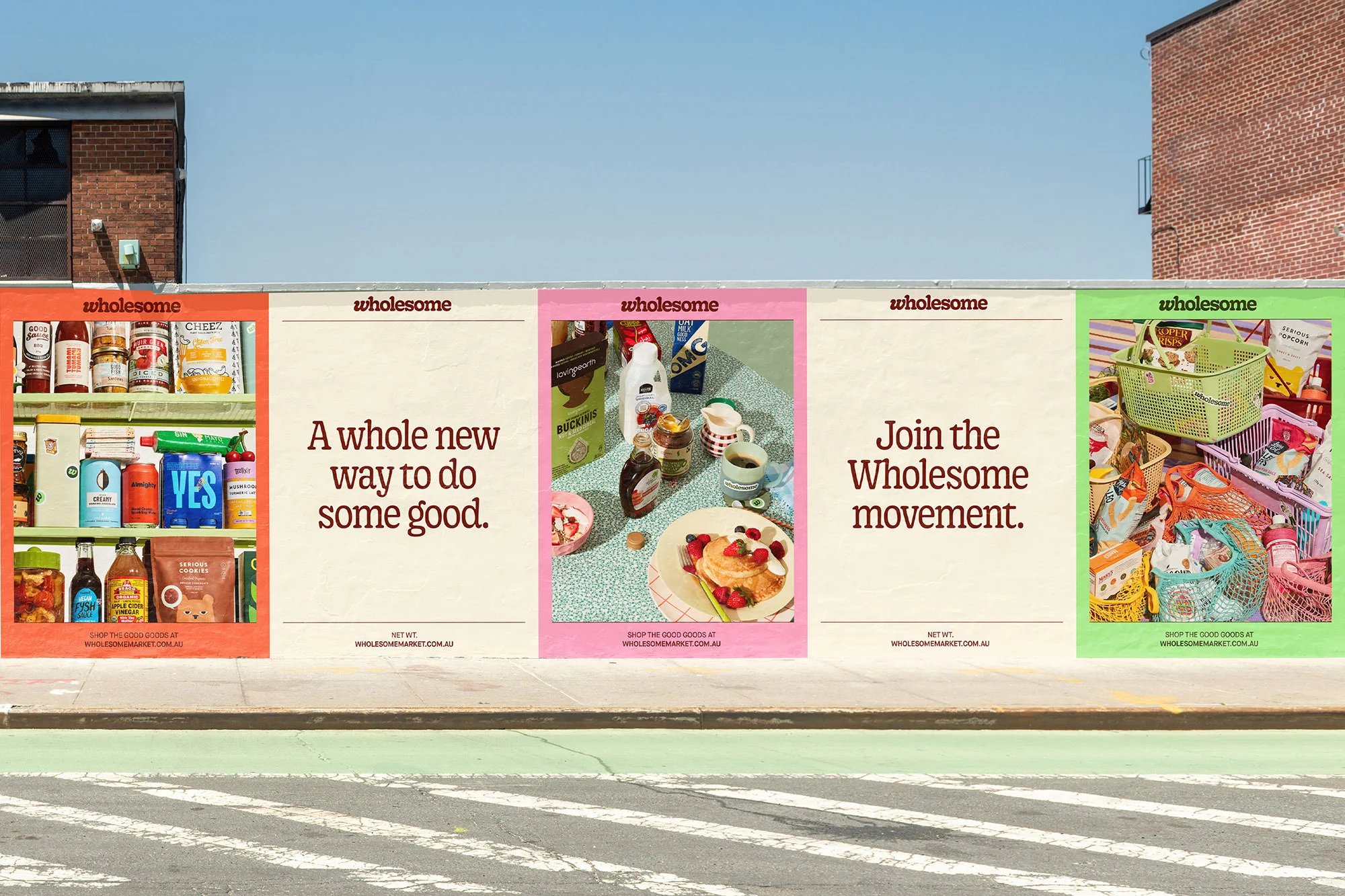 Outdoor advertising billboards showcase assorted food products and promote the Wholesome brand on a city street with crosswalk.