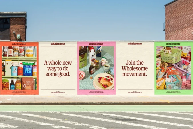 Outdoor advertising billboards showcase assorted food products and promote the Wholesome brand on a city street with crosswalk.