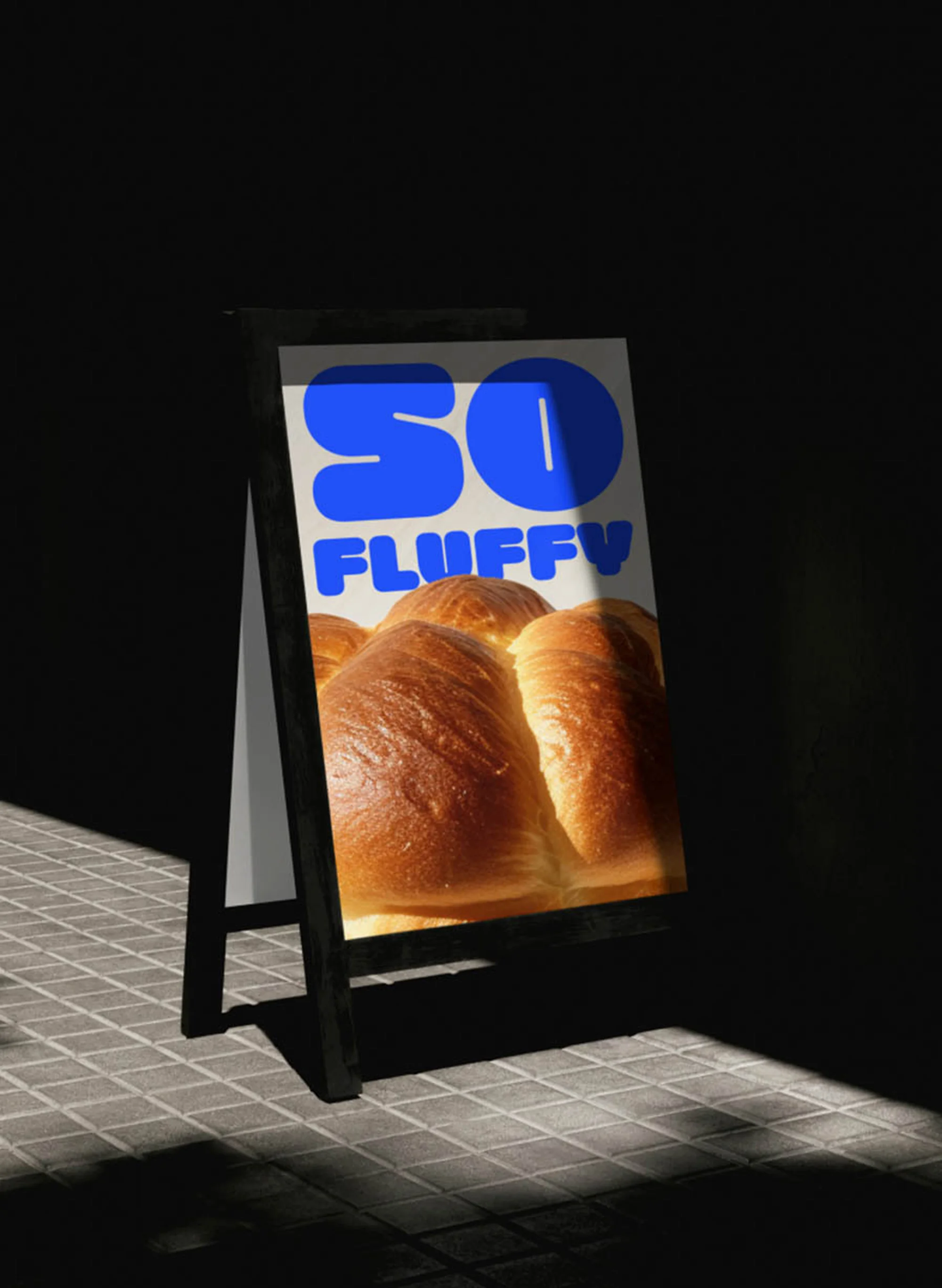A-frame sign with a poster featuring a loaf of bread and the text 'SO FLUFFY' is positioned on a tiled surface with stark lighting.