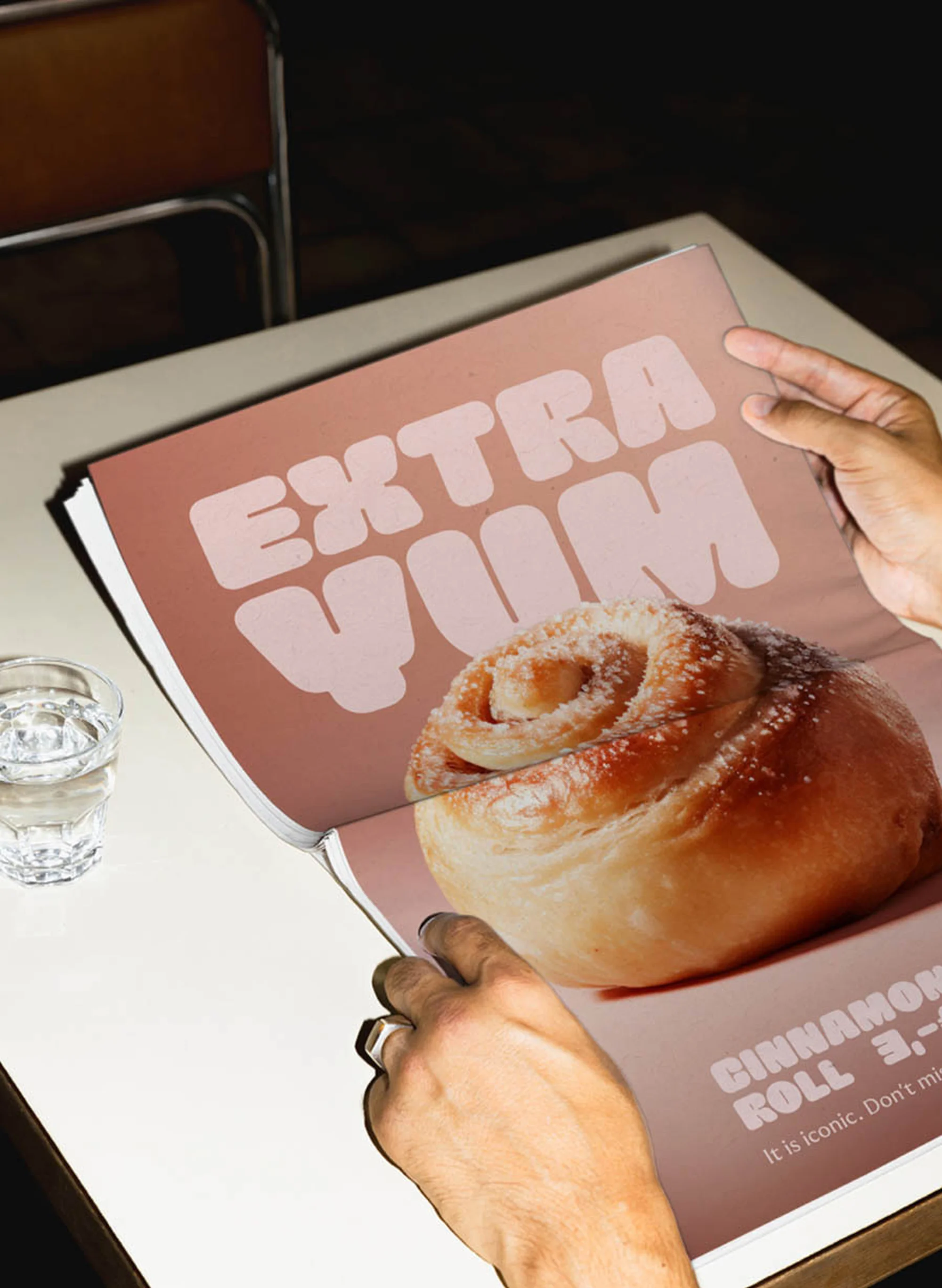 Close-up of a cinnamon roll advertisement being held by a person, featuring the text 'Extra Yum' in a well-lit, indoor setting.
