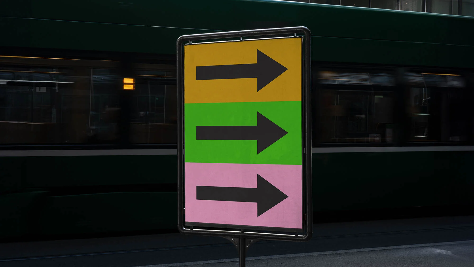 Directional sign with arrows in yellow, green, and pink with a blurred train in the background. The arrows indicate direction.