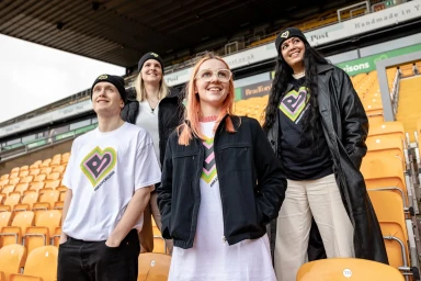 Four people standing in a stadium wearing matching branded shirts and beanies with heart graphics