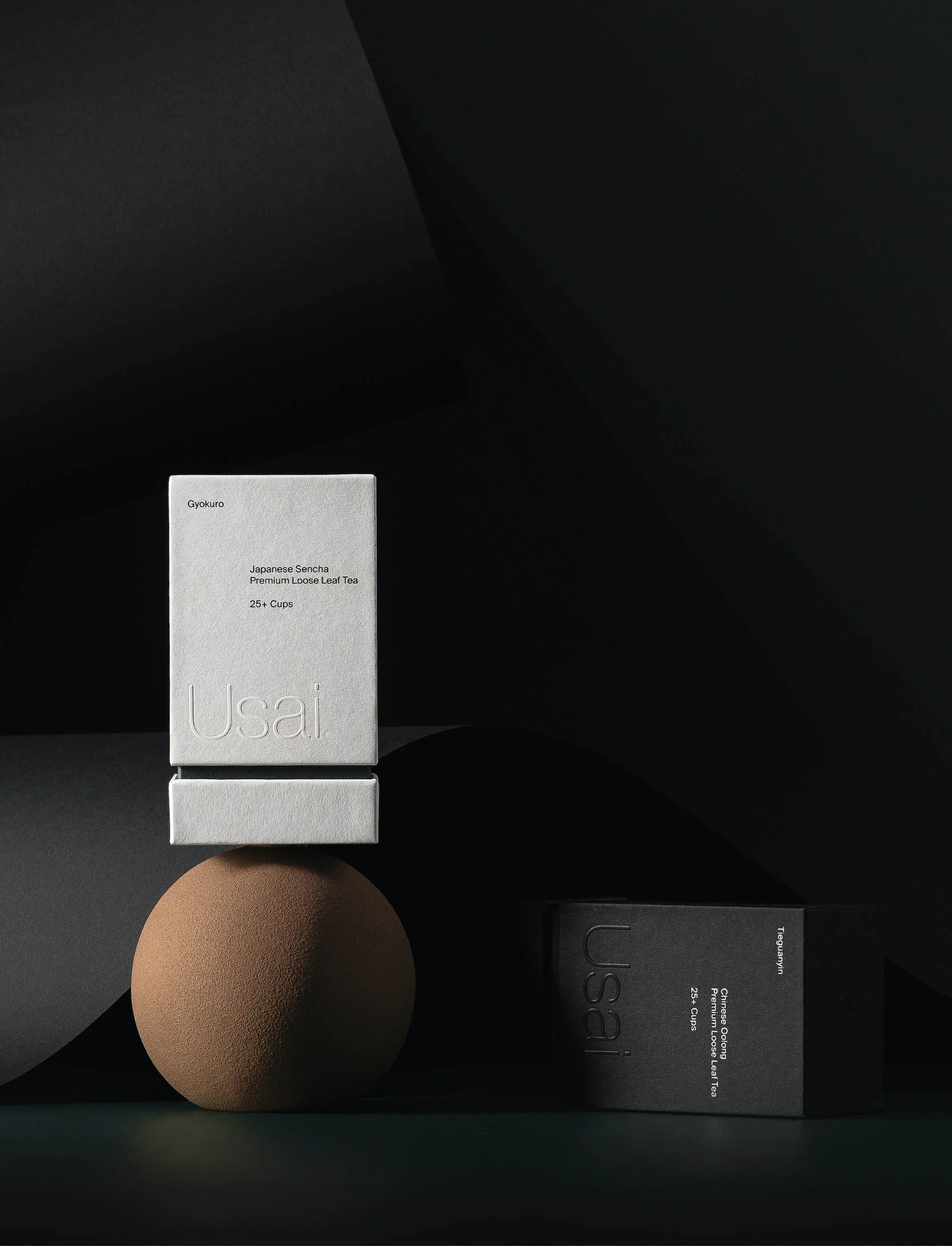 Two boxes of Usai Japanese Sencha Premium Loose Leaf Tea are stacked on a brown sphere against a black background in a product shot.
