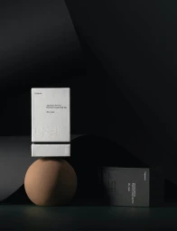 Minimalist product packaging for Usai tea featuring a white box balanced on a brown sphere against a black backdrop