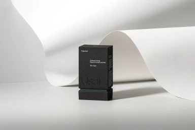 A black tea packaging box with white typography standing upright on a curved white paper sweep background