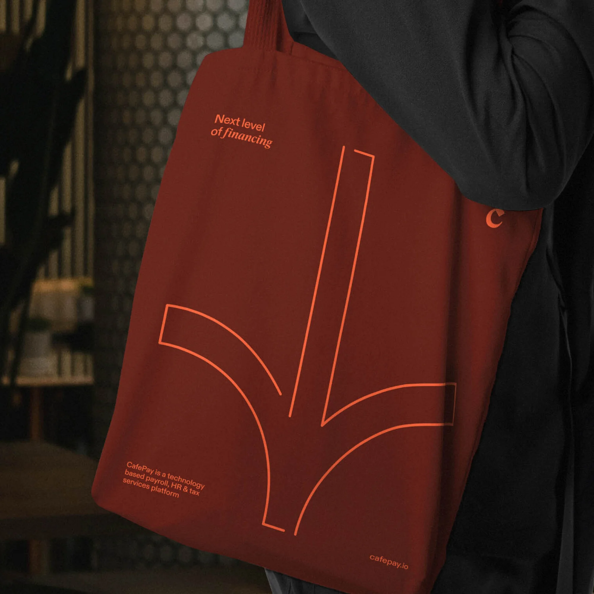 A person is holding a dark red tote bag with a light red arrow design pointing downwards, alongside text about financial technology.