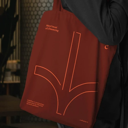A person is holding a dark red tote bag with a light red arrow design pointing downwards, alongside text about financial technology.