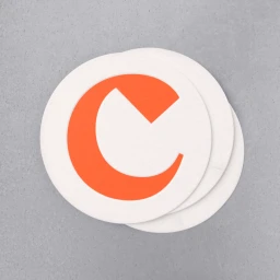 Three round white coasters featuring a bold orange letter C logo layered on a textured grey concrete surface