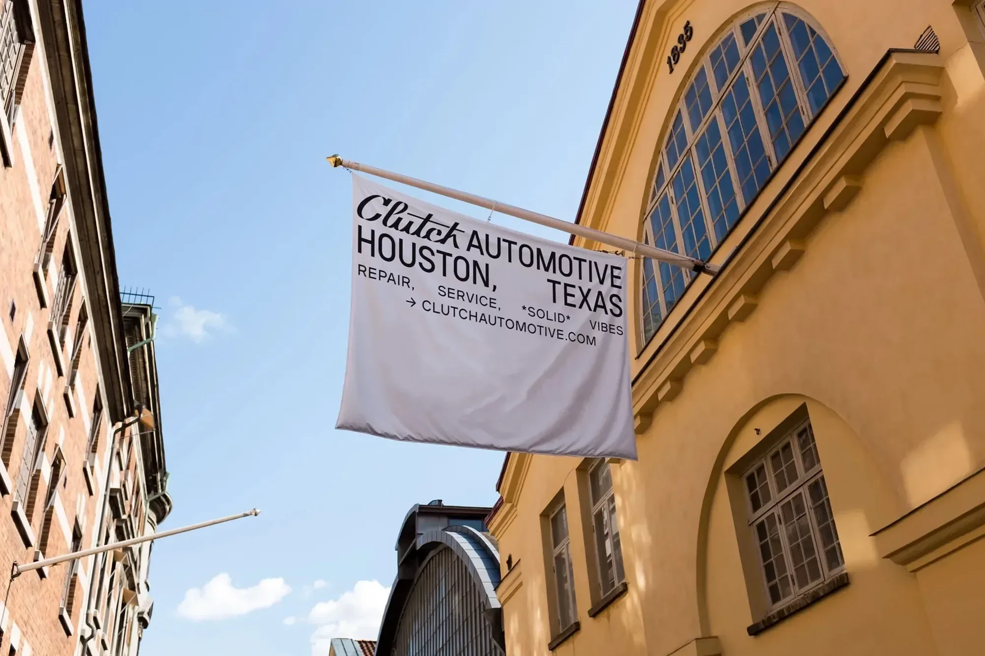 Clutch Automotive advertisement banner on a yellow brick building under a bright blue sky. City building in the background.