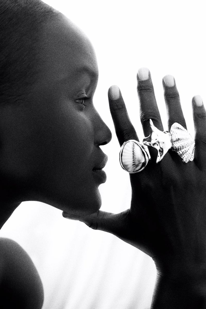Close-up black and white portrait of a Black woman with statement shell rings on her hand, set against a bright white background.