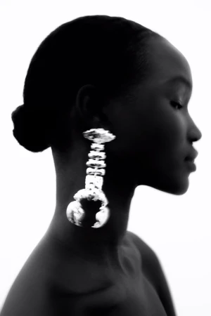 Portrait of a Black woman in profile wearing a large silver statement earring against a white background in a photo studio.