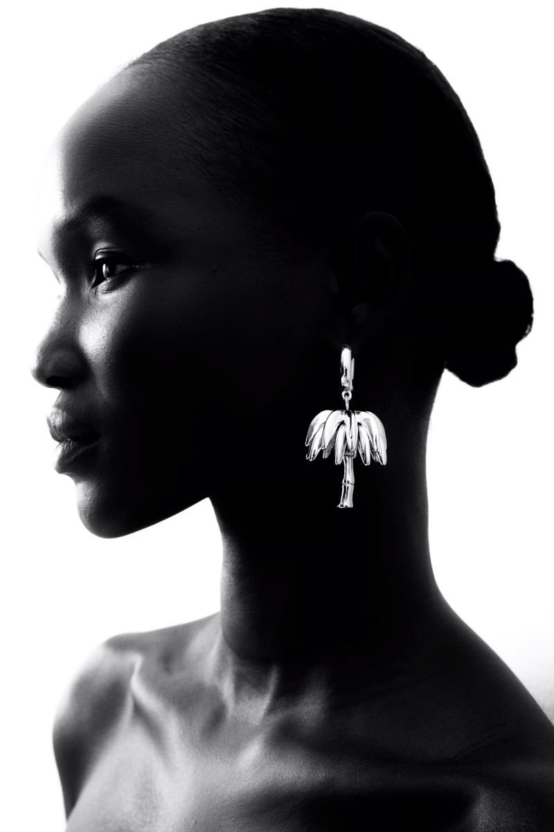Monochrome portrait of a Black woman in profile wearing palm tree earrings against a bright white background in a studio setting.