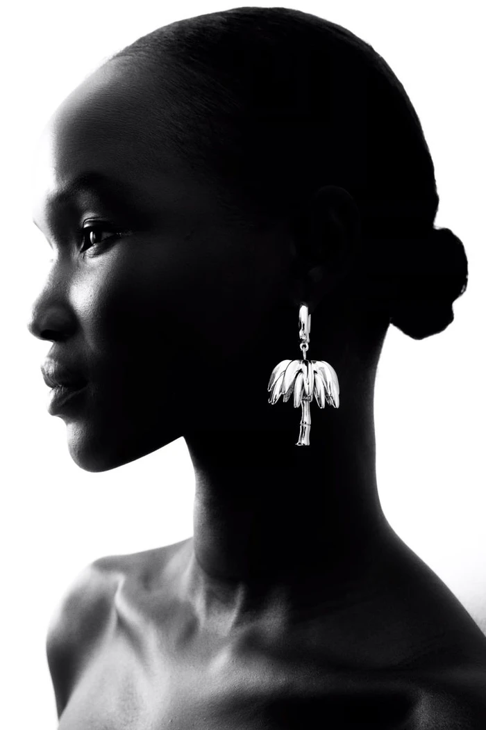 Profile silhouette of a Black model wearing a metallic palm tree earring against a bright white background
