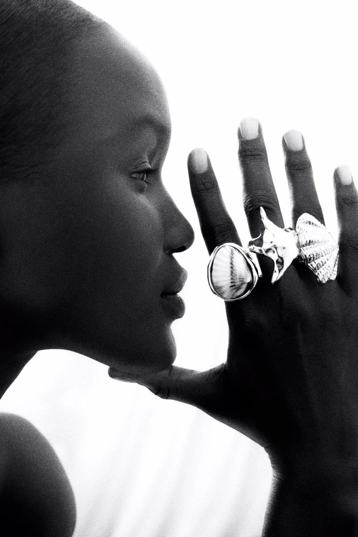Close-up profile of a black woman wearing bold silver shell rings on her hand against a white background