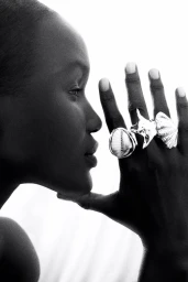 Close-up profile of a black woman wearing bold silver shell rings on her hand against a white background