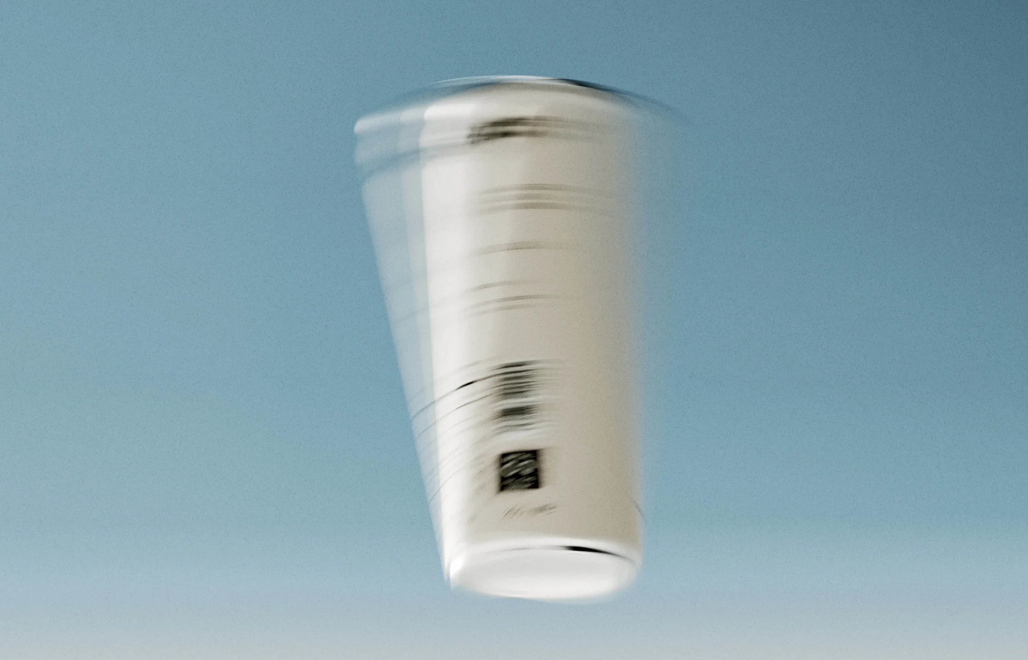 A blurred image of a white paper cup with printed details against a solid blue background. Shot with motion blur to convey movement.