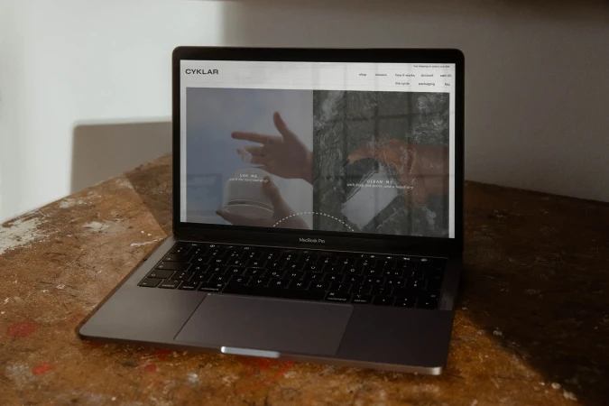 Laptop displaying Cyklar website, showcasing hands and a minimalist design, set on a textured wooden surface with natural lighting.