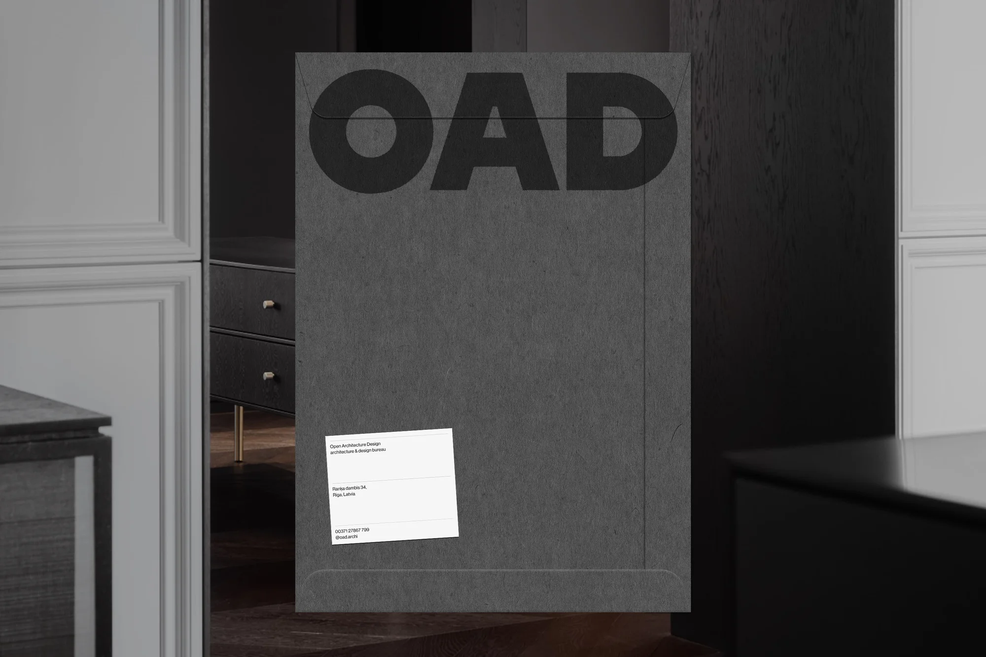 Grey portfolio with black lettering 'OAD' displayed in an indoor setting with black furniture and a white business card attached.