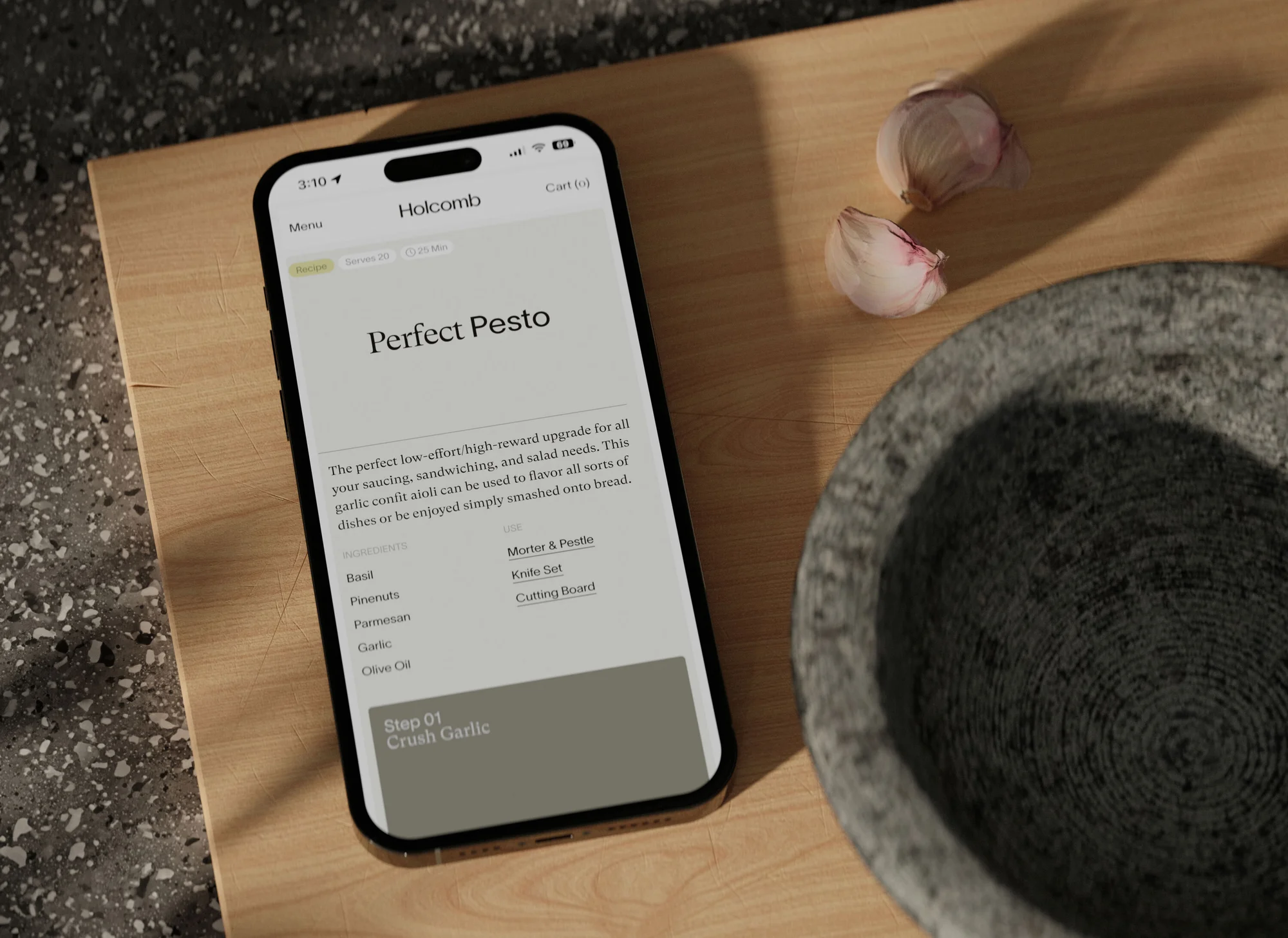 Overhead shot of a smartphone displaying a pesto recipe, alongside garlic cloves and a stone mortar on a wooden cutting board.