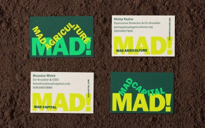 Four business cards for Mad Agriculture and Mad Capital arranged flat on a textured dark brown soil background.