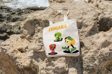 Canvas tote bag with retro cartoon fruit illustrations resting on rough rocky terrain outdoors