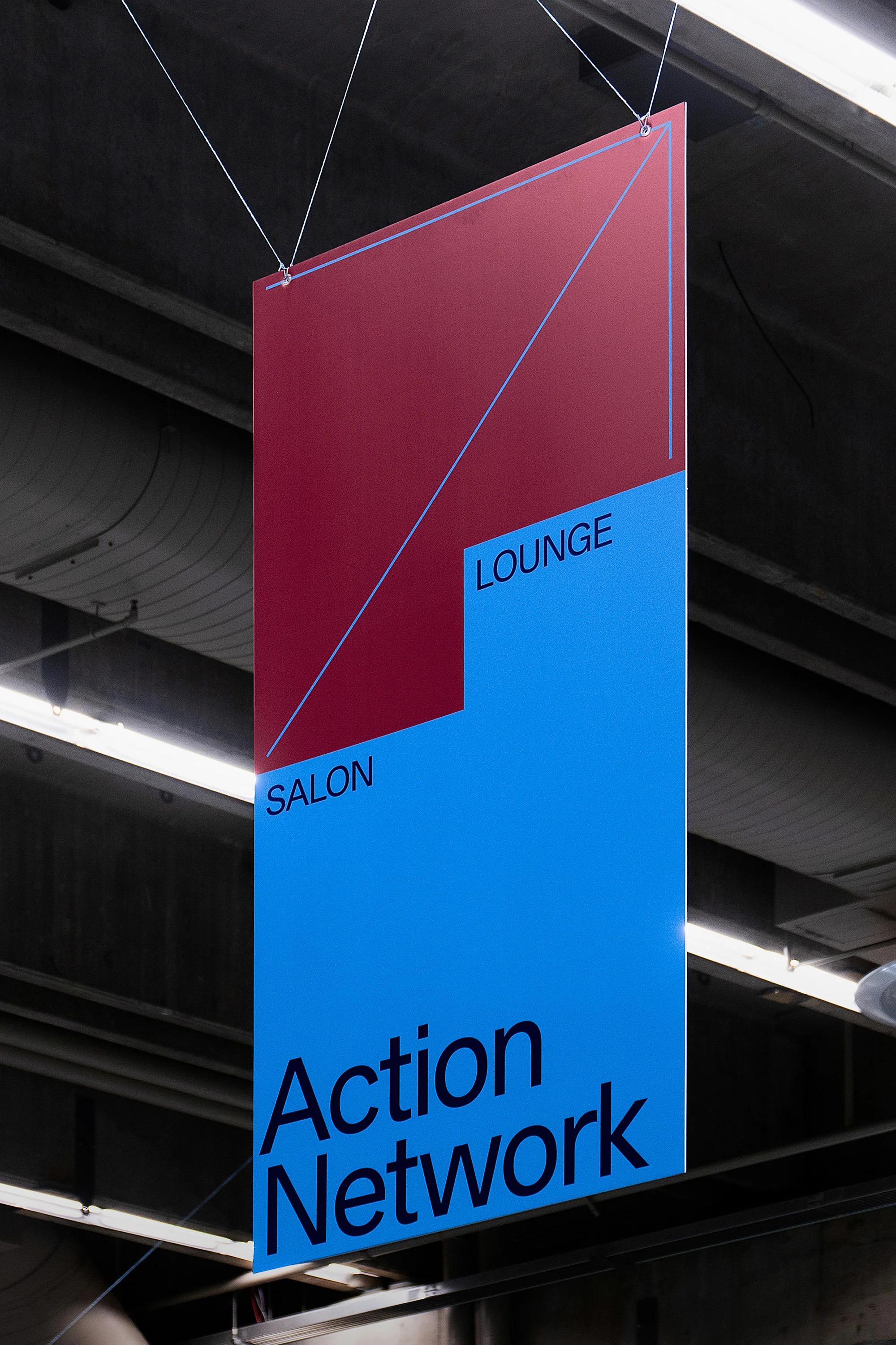 Geometric signage hanging from the ceiling features Salon and Lounge above Action Network, displayed in bold blue and burgundy.