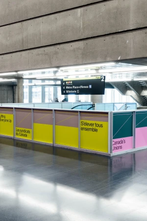 Indoor public transit station area with colorful graphic panels featuring text in both English and French, and overhead directional signs.