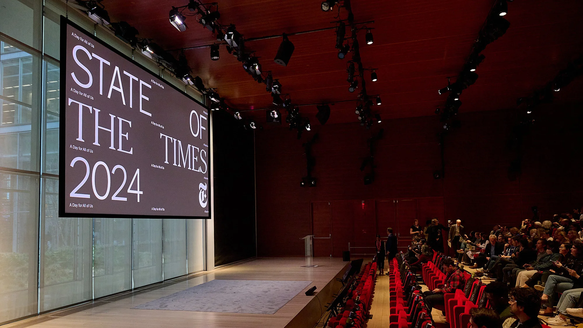 Large screen displaying 'State of the Times 2024' in an auditorium with rows of seated people facing the stage, indoor event.