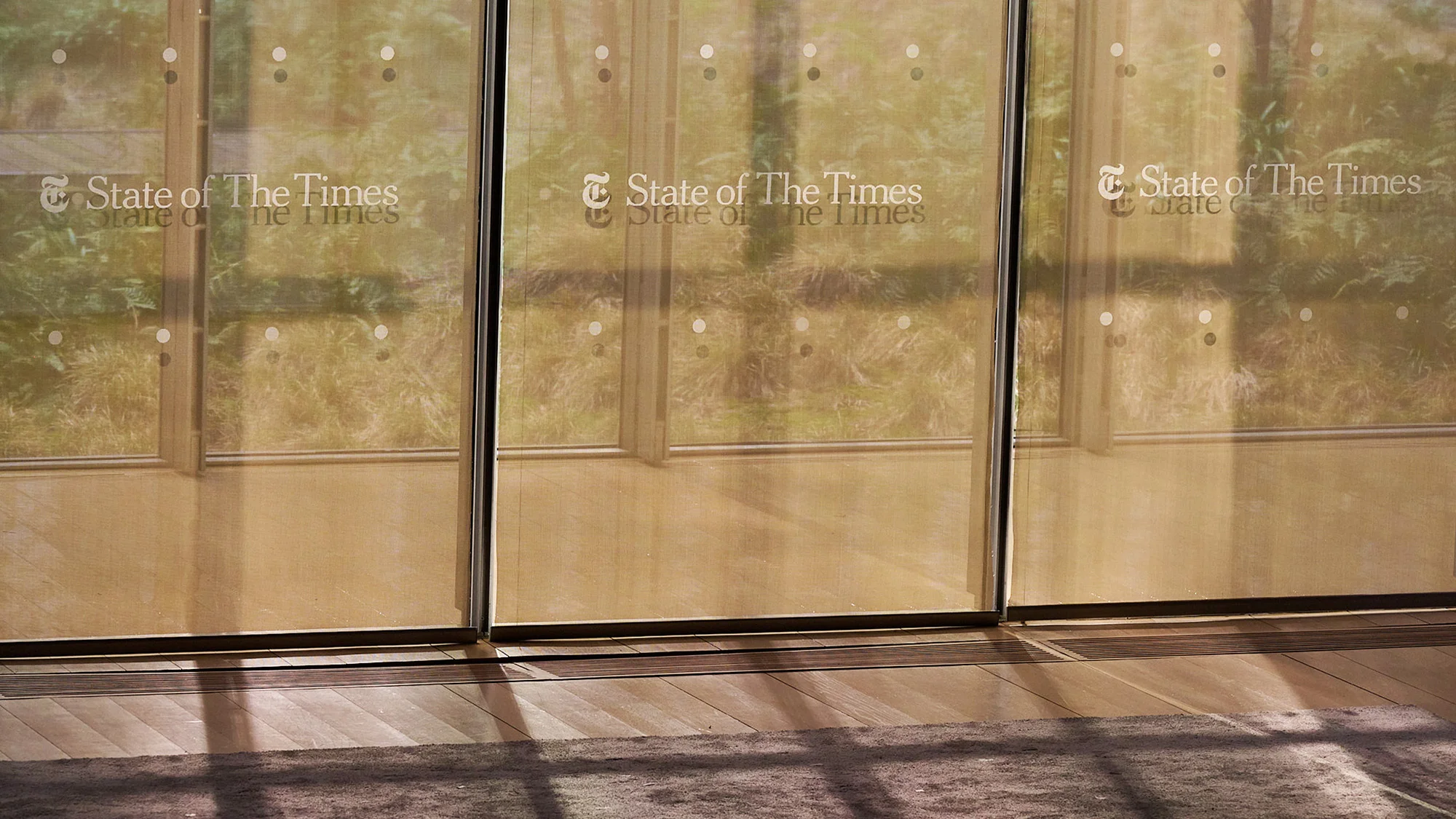 View of glass doors with the text 'State of The Times' printed on them, along with a glimpse of trees outside.