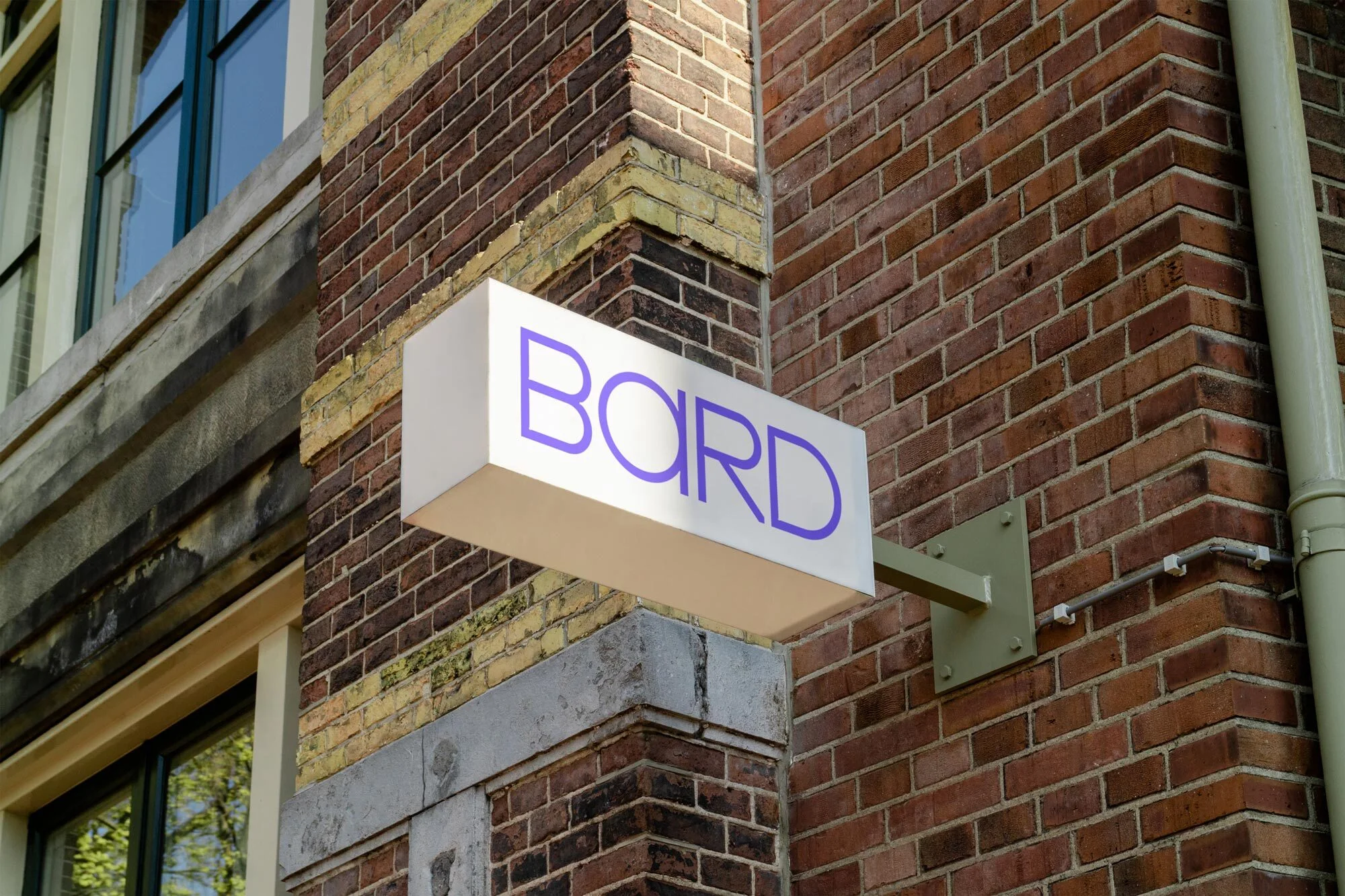 Exterior of brick building with white sign displaying the word 'BARD' in purple lettering, architectural details, and window reflections.