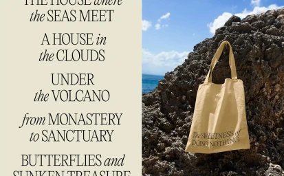 Beige tote bag hanging on dark coastal rock with ocean and cloudy sky in background next to typographic text panel.