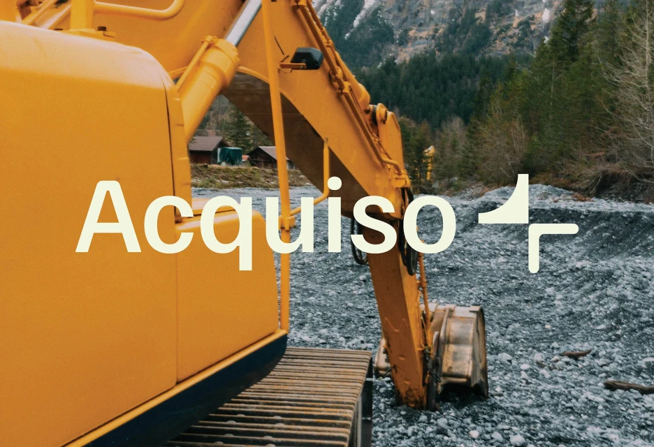 Yellow excavator at a rocky construction site with a backdrop of evergreen trees and mountains; text overlay says "Acquiso".