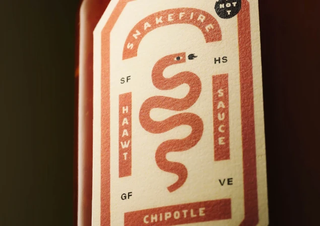 Close-up of 'Snakefire' chipotle hot sauce label with a stylized snake design and bold typography on a light beige background.