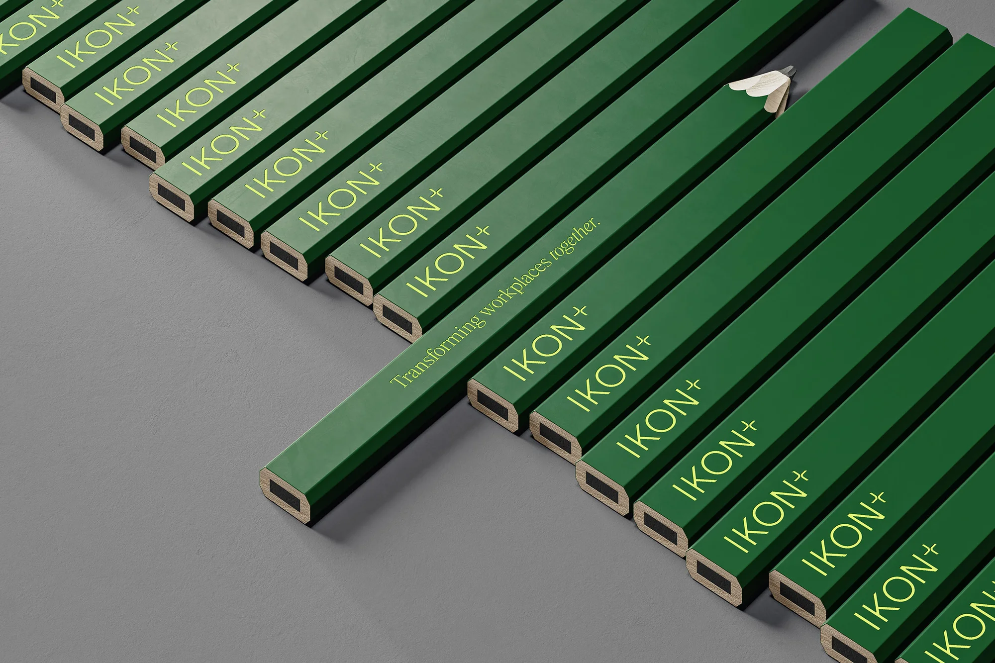 Elevated studio shot featuring aligned green pencils, each branded with 'IKON+' in yellow, set against a flat gray background.
