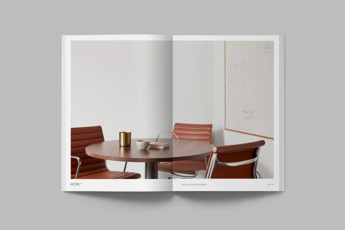 Interior design publication displays a minimalist office space with a round conference table, brown leather chairs, and a whiteboard.