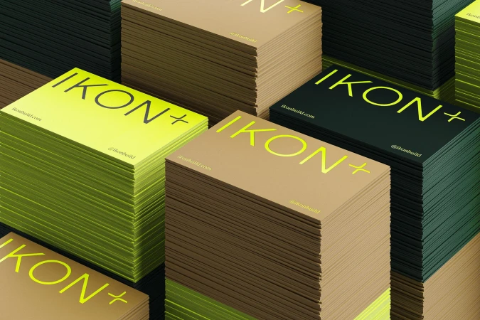 Stacks of modern business cards in shades of green, brown, and black, displaying the company name 'IKON+' with website and social details.