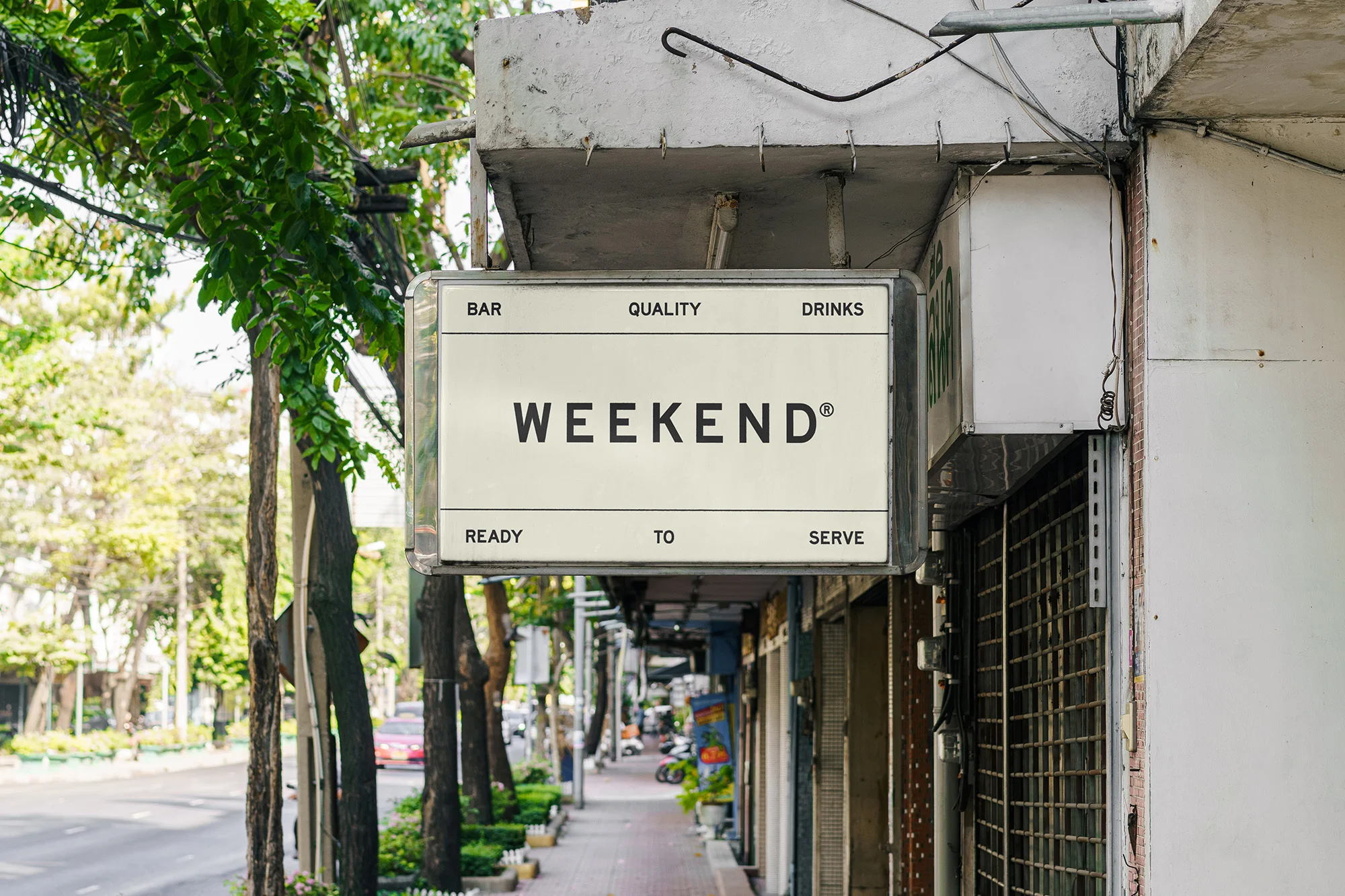 Illuminated sign with 'WEEKEND' displayed, promoting a bar with quality drinks, mounted on a building exterior with trees nearby.