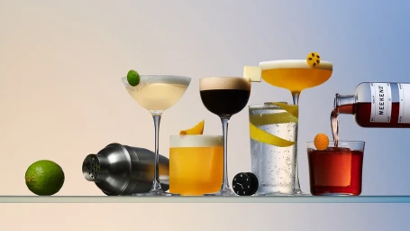 A collection of various cocktails, a cocktail shaker, and a bottle pouring liquid into a glass on a gradient background