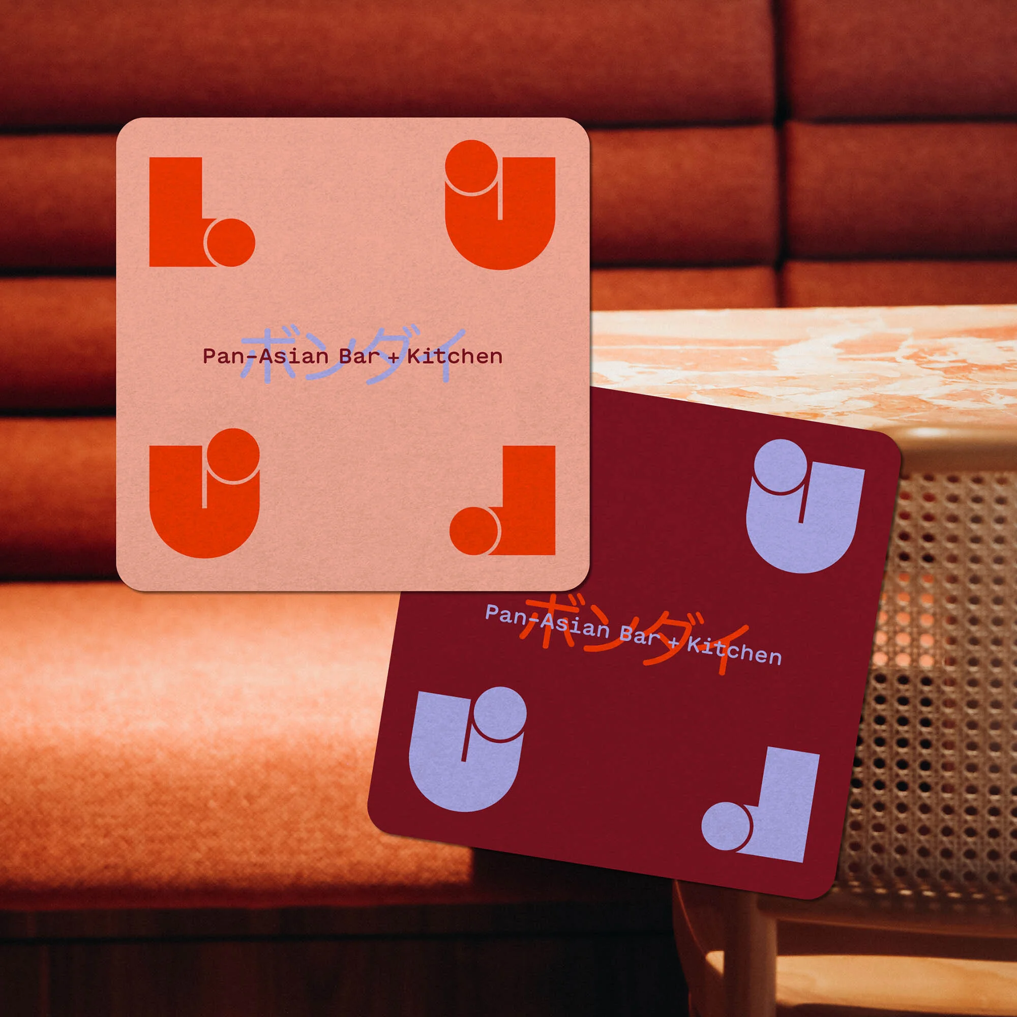 Two square coasters displaying the logo for a Pan-Asian bar and kitchen are set against a textured orange background.