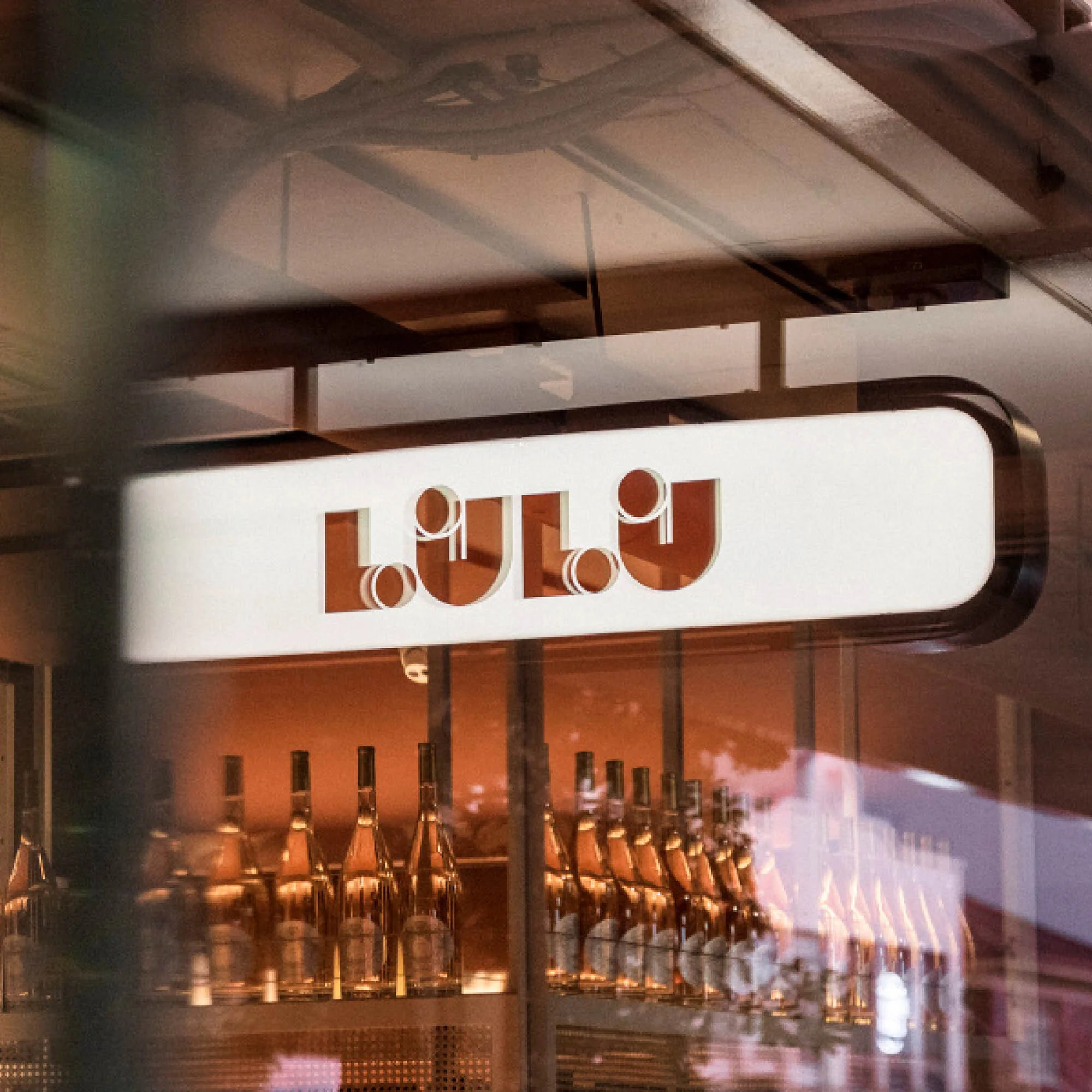 Illuminated 'Lulu' sign above a shop window displays rows of wine bottles, with a warm, inviting ambiance.